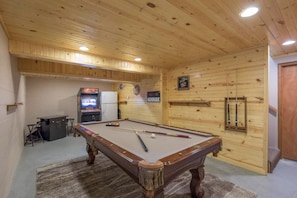 Enjoy a game of pool in this room featuring a pool table, bar area with refrigerator and TV, and a cozy atmosphere.