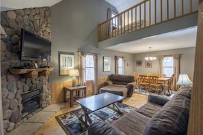 Relax in this stylish living area with a high ceiling, stone accent wall, and cozy fireplace. Enjoy the flat-screen TV and comfortable seating for a perfect evening in.