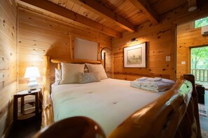 Una habitación de cabaña de madera con una cama, una mesita de noche, un cuadro enmarcado y una ventana.