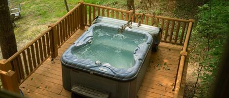 Ein Whirlpool auf einer Holzterrasse, umgeben von Bäumen.