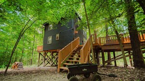 A cabin with a wooden deck and stairs, surrounded by trees.