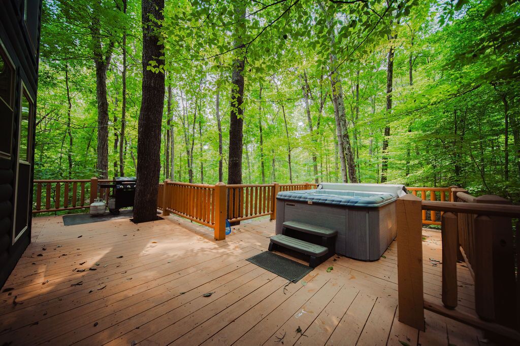Eine Holzterrasse mit einem Whirlpool, umgeben von einem Wald.