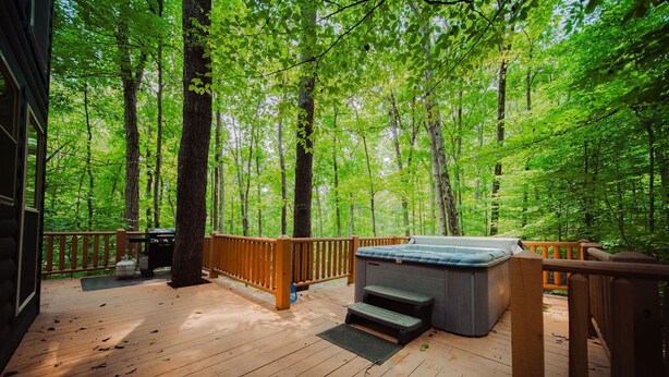 A wooden deck with a hot tub, surrounded by a forest.