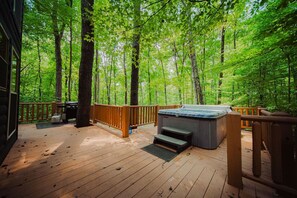 Eine Holzterrasse mit einem Whirlpool, umgeben von einem Wald.