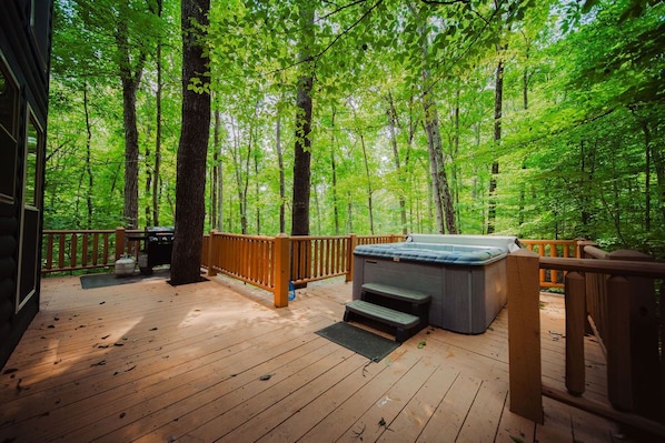 A wooden deck with a hot tub, surrounded by a forest.