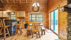 A wooden cabin interior with a dining area, stone fireplace, and large windows. - Sieri Glen Cabin | Hocking Hills, Sleeps 14 (Logan)