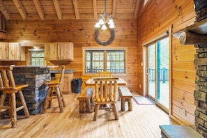 A wooden cabin interior with a stone fireplace, wooden dining table, and chairs. - Sieri Glen Cabin | Hocking Hills, Sleeps 14 (Logan)