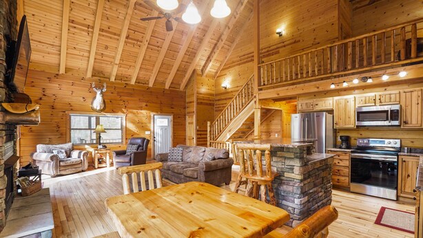 A spacious wooden cabin with a dining area, living room, kitchen, and a staircase leading to an upper level. - Sieri Glen Cabin | Hocking Hills, Sleeps 14 (Logan)