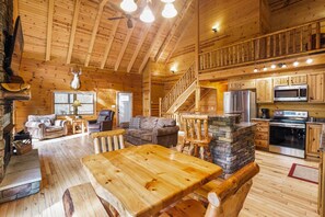 A spacious wooden cabin with a dining area, living room, kitchen, and a staircase leading to an upper level.