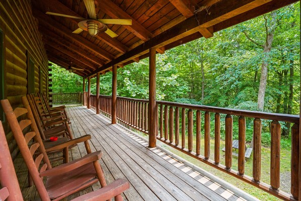 A wooden deck with benches, a railing, and a view of a forest.