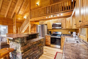 A spacious kitchen with wooden cabinets, a stone island, stainless steel appliances, and a wooden staircase.