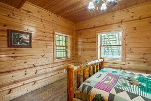 Une pièce de style cabane en bois, avec un lit, deux fenêtres et un tableau encadré au mur.