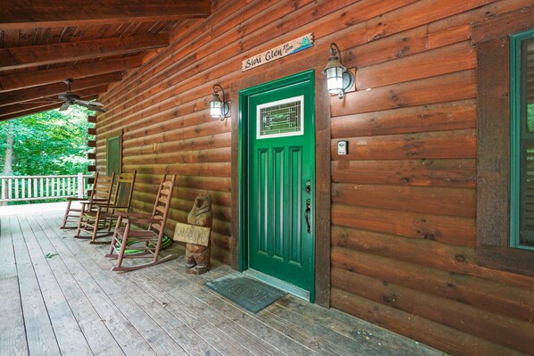 Une cabane en bois avec une porte verte, des fauteuils à bascule et une enseigne indiquant « Sioni Glen ».
