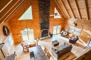 A spacious cabin with a stone fireplace, wooden floors, and a high ceiling.