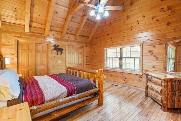 A wooden cabin bedroom with a bed, dresser, and a ceiling fan.
