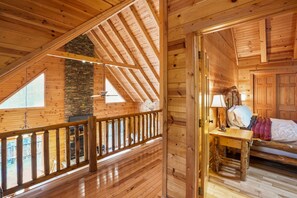 A wooden interior with a sloped ceiling, a stone fireplace, and a wooden bed with a nightstand.