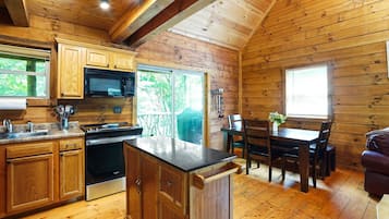 A wooden cabin interior with a kitchen, dining area, and a fireplace.