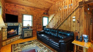 Interior acogedor de una cabaña con chimenea de piedra, sofá de cuero y escalera de madera.