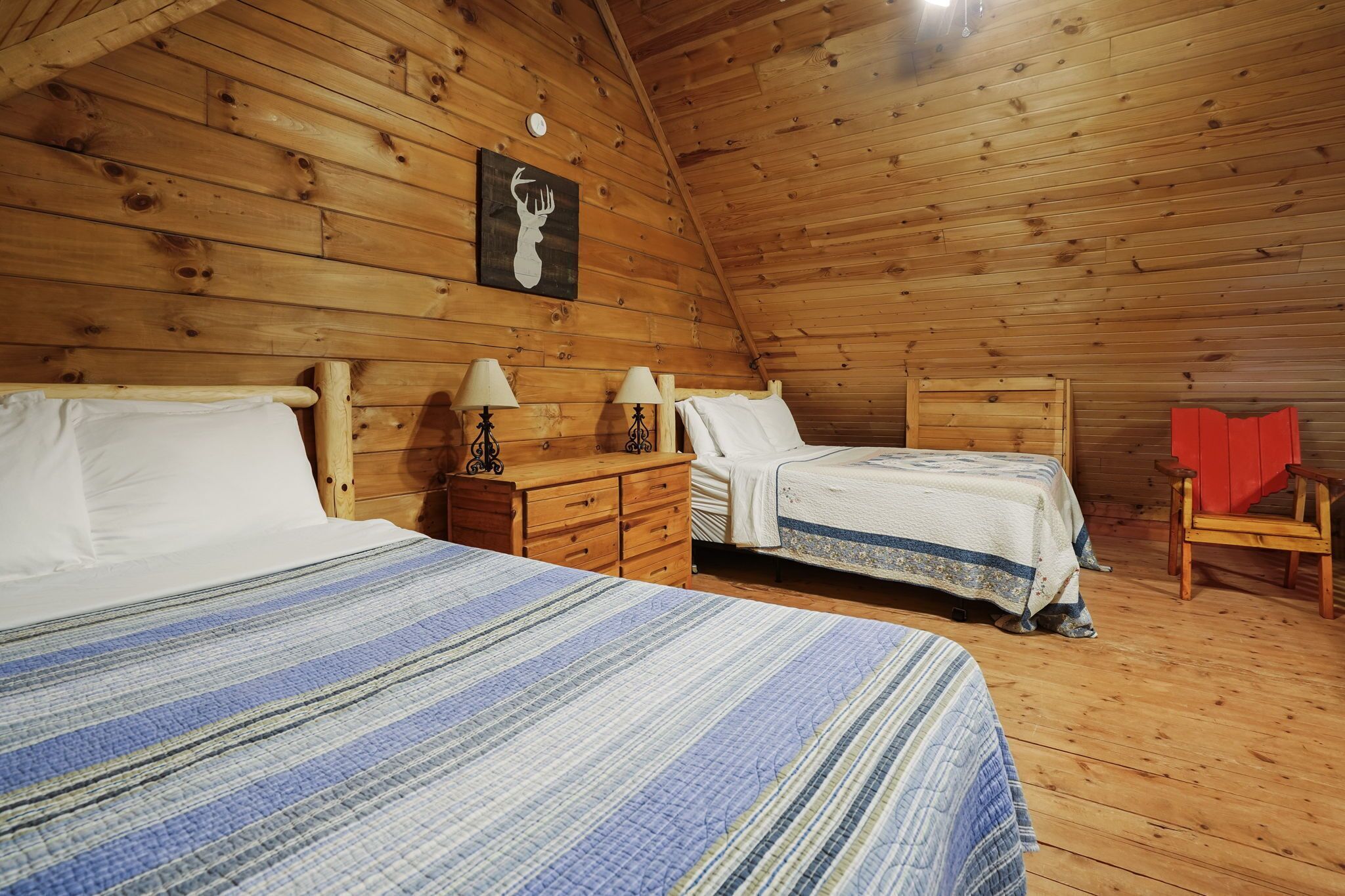 Ein Schlafzimmer einer Holzhütte mit zwei Betten, einem Nachttisch, einer Lampe und einem roten Sessel.