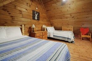A wooden cabin bedroom with two beds, a nightstand, a lamp, and a red chair.