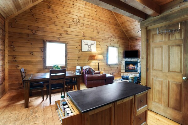 A cozy cabin interior with a wooden interior, a dining area, a fireplace, and a large wooden door.