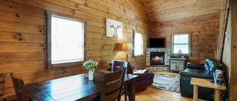 A cozy cabin interior with a wooden dining table, chairs, a fireplace, a television, and a sofa.