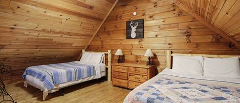 Un dormitorio estilo ático acogedor con dos camas, paredes de madera, ventilador de techo y una lámpara de pared.