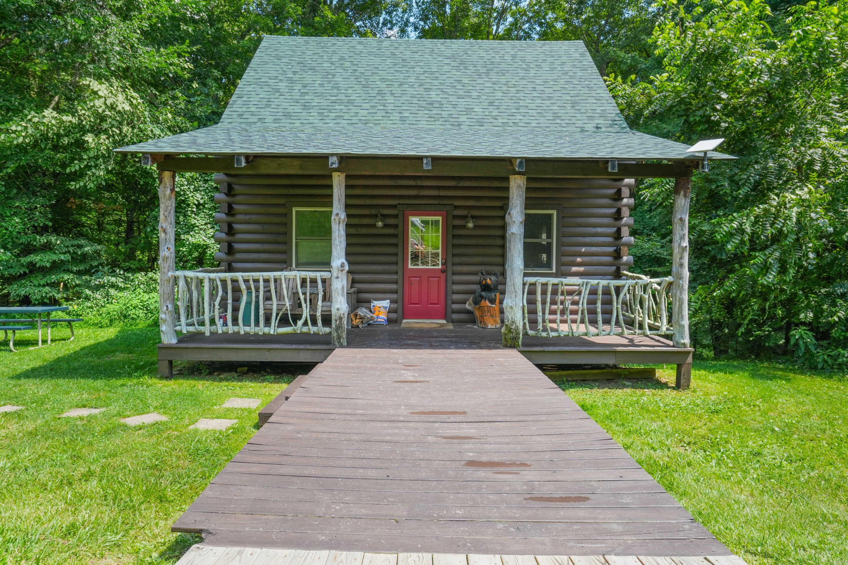 A log cabin with a porch, a red door, and a wooden walkway leading to it.