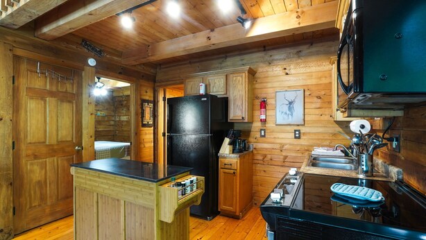 Una cocina de estilo cabaña de madera con un refrigerador negro, armarios de madera, una isla de madera con un fregadero y un microondas.