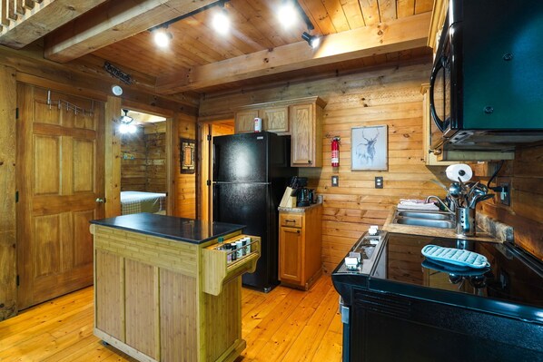 Una cocina de estilo cabaña de madera con un refrigerador negro, armarios de madera, una isla de madera con un fregadero y un microondas.