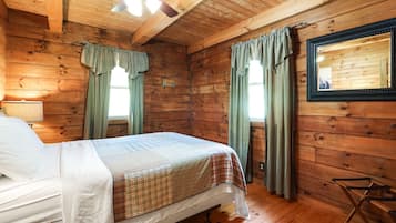A wooden cabin room with a bed, a mirror, and a ceiling fan.