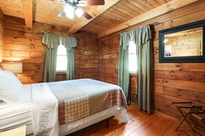 A wooden cabin room with a bed, a mirror, and a ceiling fan.