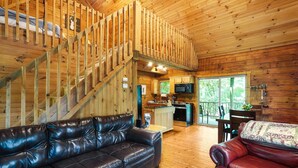 Una cabaña amplia con interior de madera, un sofá de cuero, un comedor y una cocina.