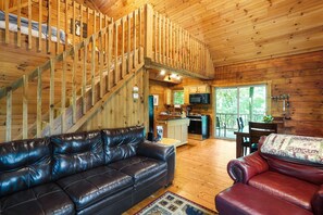 A spacious cabin with a wooden interior, a leather sofa, a dining area, and a kitchen.