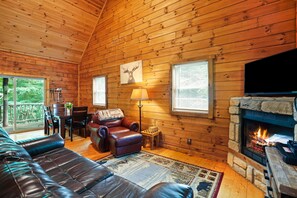 A cozy log cabin interior with a leather sofa, a fireplace, and a dining area.