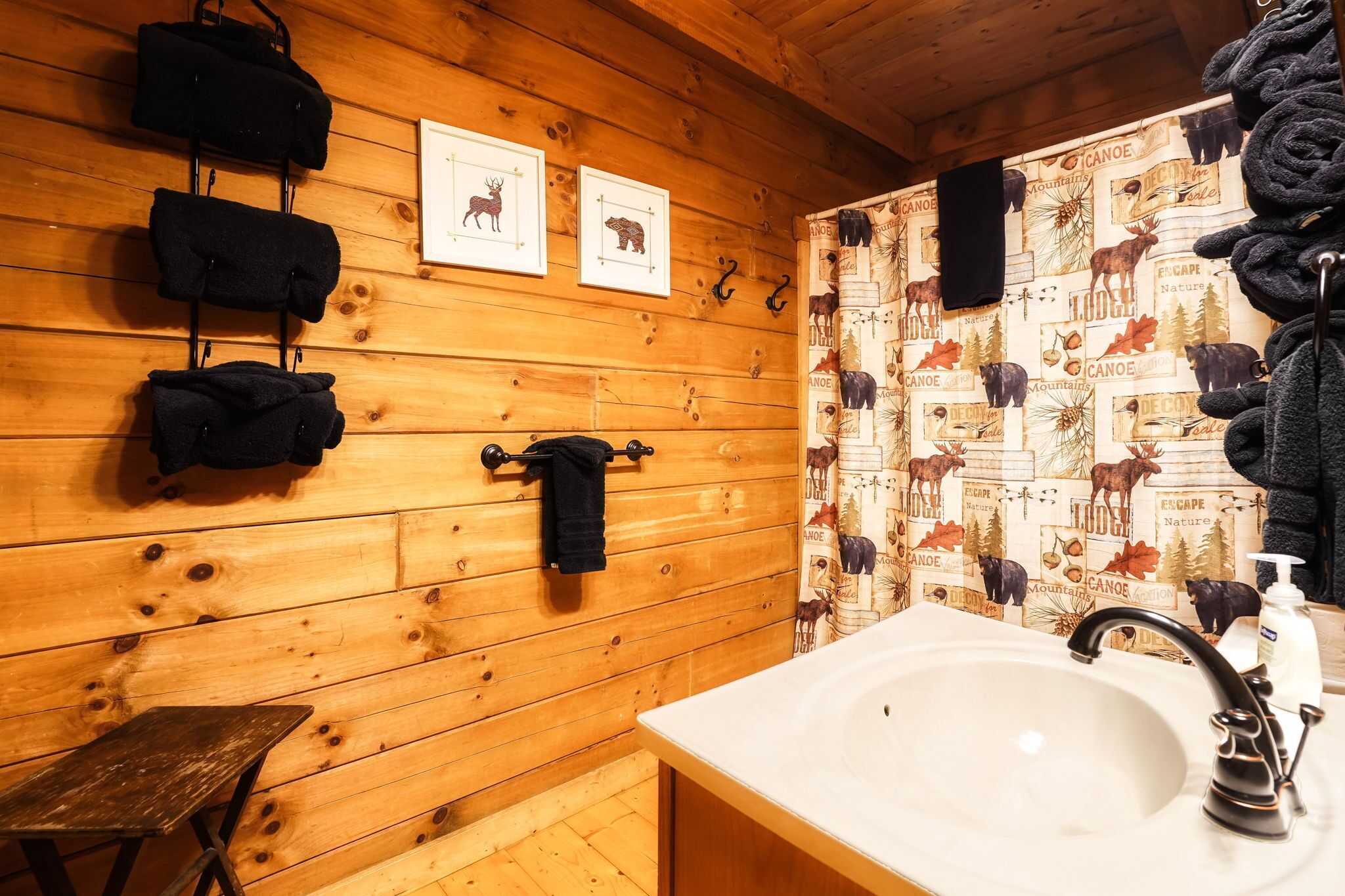 L’intérieur d’une cabane en bois, avec un évier blanc, des murs en bois et un rideau de douche décoré sur le thème de la cabane.