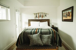 A bedroom with a bed, pillows, a bedside table, a lamp, a wall-mounted plant, and a framed picture. - The Cowboy Inn - Luxury Bozeman (Bozeman)