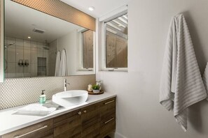A modern bathroom with a large mirror, a white sink, wooden cabinets, and a towel hanging on the wall. - The Cowboy Inn - Luxury Bozeman (Bozeman)