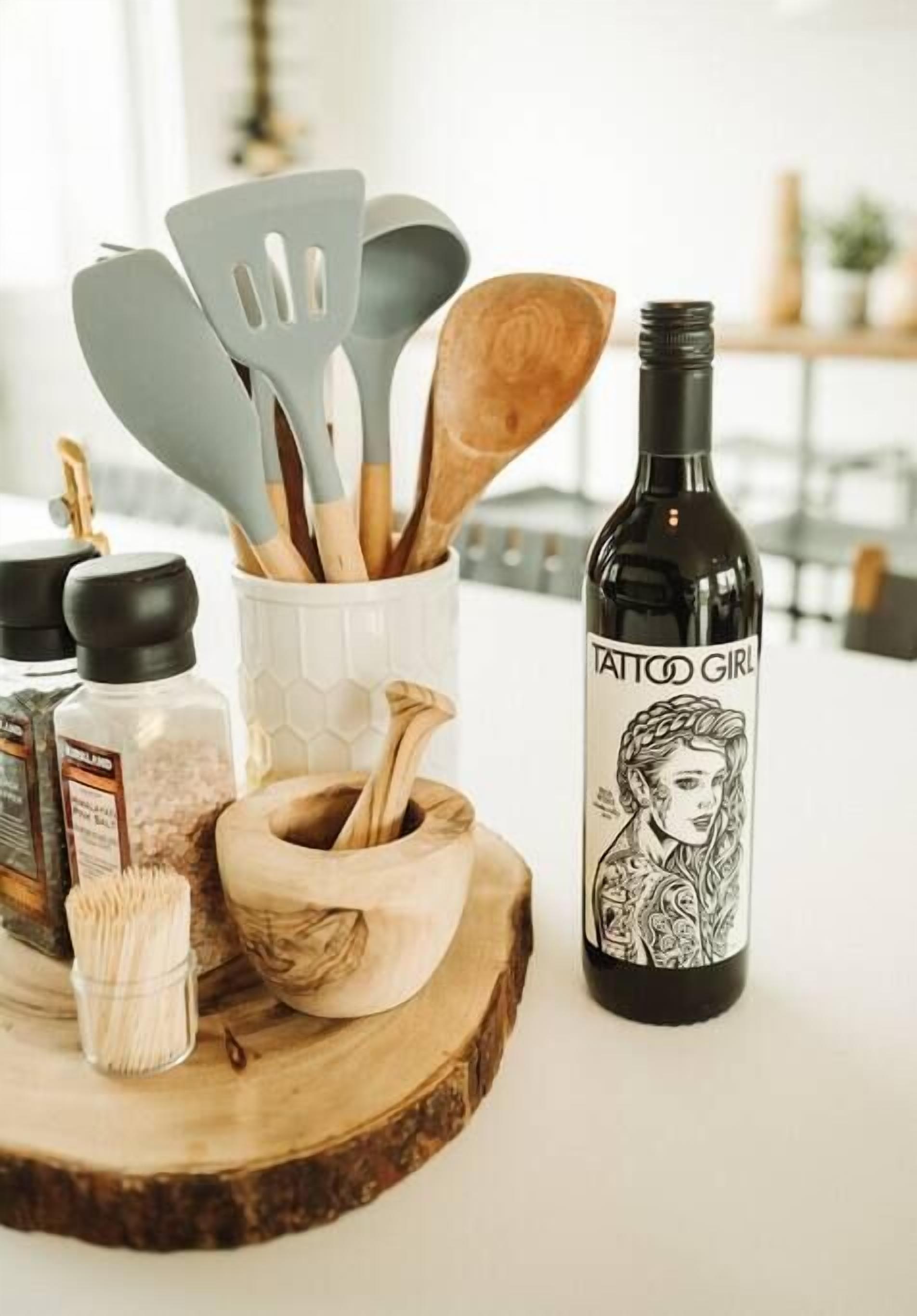 A kitchen counter with a bottle of wine, a wooden cutting board, and various kitchen utensils.