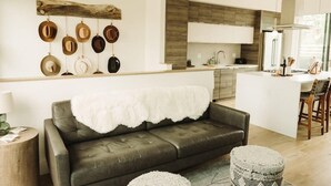 A modern kitchen with a central island, a dining area with a white table and chairs, and a living area with a sofa and ottoman. - The Cowboy Inn - Luxury Bozeman (Bozeman)