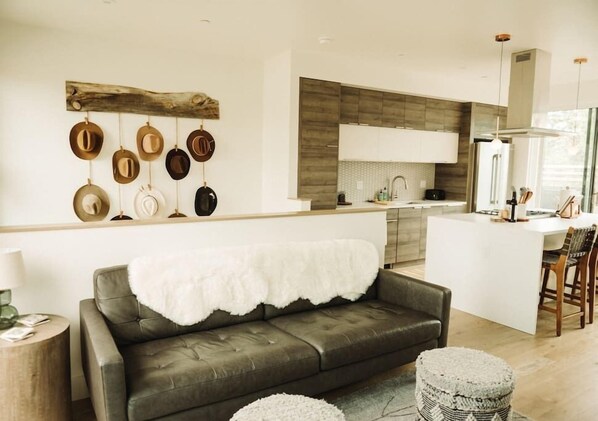A modern kitchen with a central island, a dining area with a white table and chairs, and a living area with a sofa and ottoman. - The Cowboy Inn - Luxury Bozeman (Bozeman)