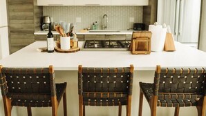A modern kitchen with a central island, three woven chairs, and a stainless steel range hood. - The Cowboy Inn - Luxury Bozeman (Bozeman)
