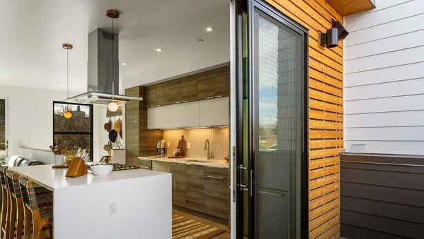 A modern kitchen with a central island, wooden wall paneling, and a sliding glass door leading to an outdoor area. - The Cowboy Inn - Luxury Bozeman (Bozeman)