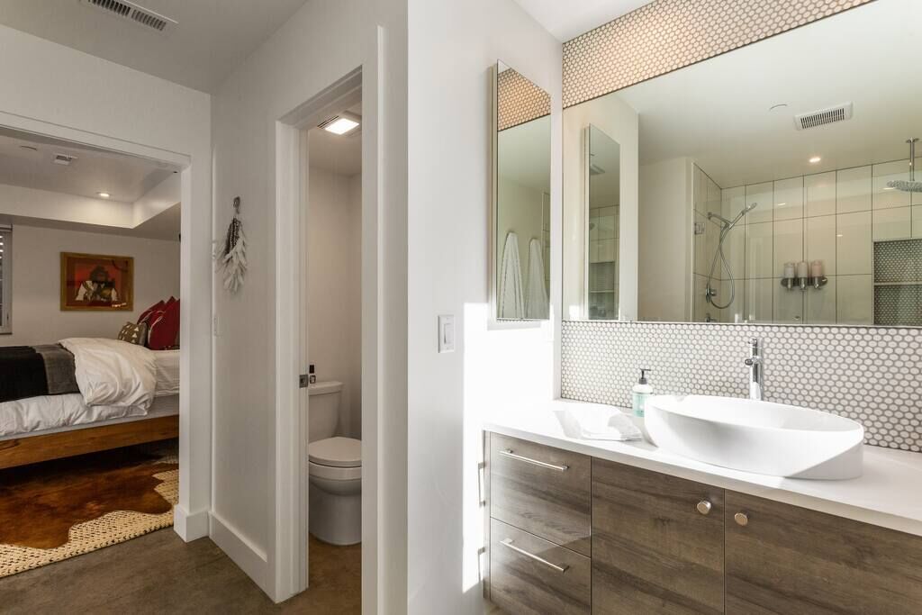 A modern bathroom with a large mirror, a white sink, and a shower.
