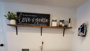 A laundry room with a front-loading washer and dryer, a shelf with jars and a sign above, and a small plant. - The White House Cottage (Inkom)