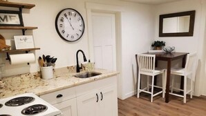 A kitchen with white cabinets, a stove, a sink, and a dining area with a chair and table. - The White House Cottage (Inkom)