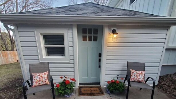 A house with a front porch featuring two chairs with floral cushions, a light fixture above the door, and a welcome mat. - The White House Cottage (Inkom)