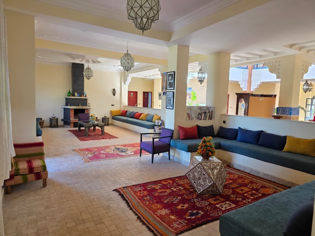 Un salón amplio con sofá, sillones y una mesa de centro. Hay alfombras decorativas en el suelo y una lámpara colgante.