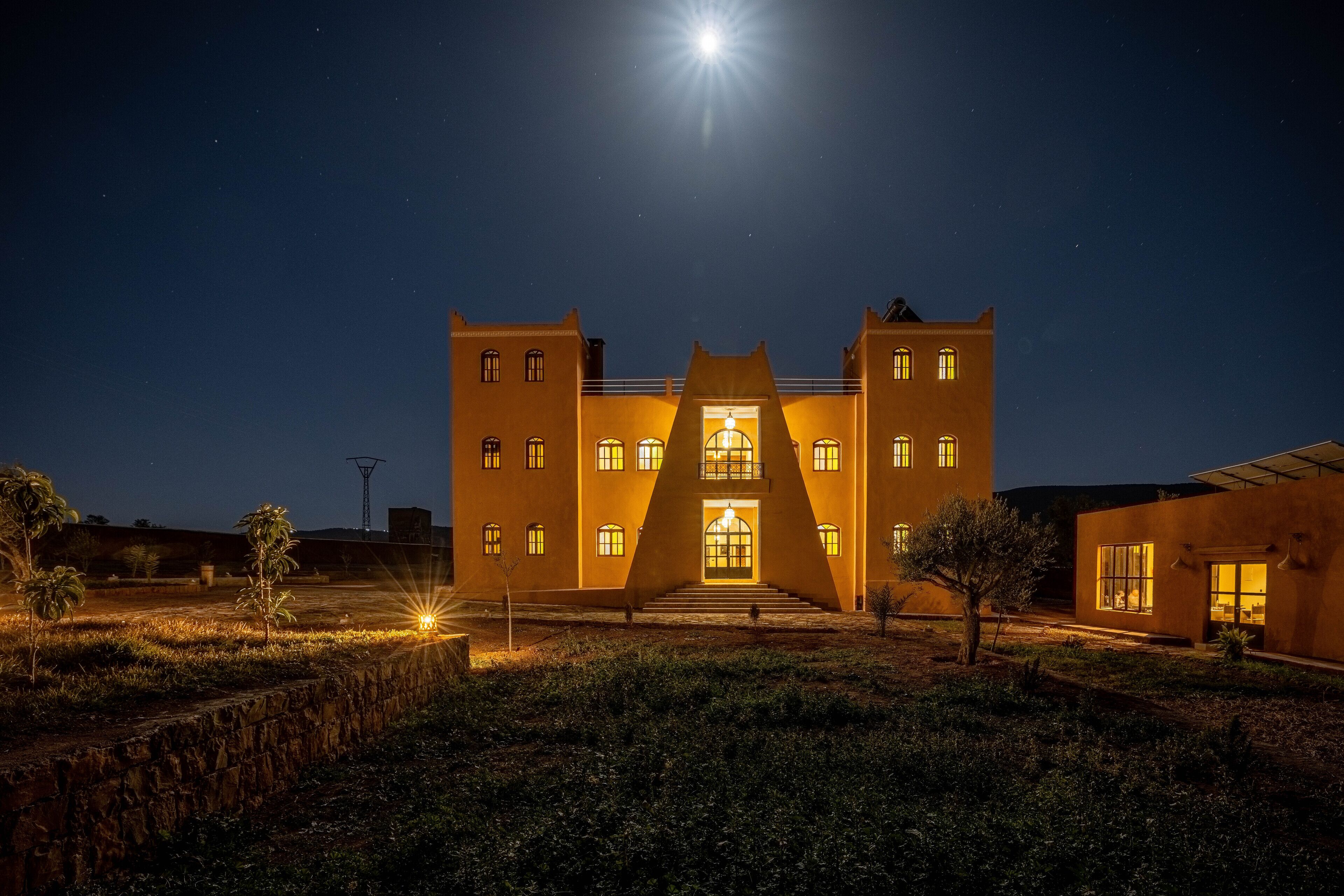 A large, symmetrical building with a central entrance, multiple windows, and a well-lit facade at night.