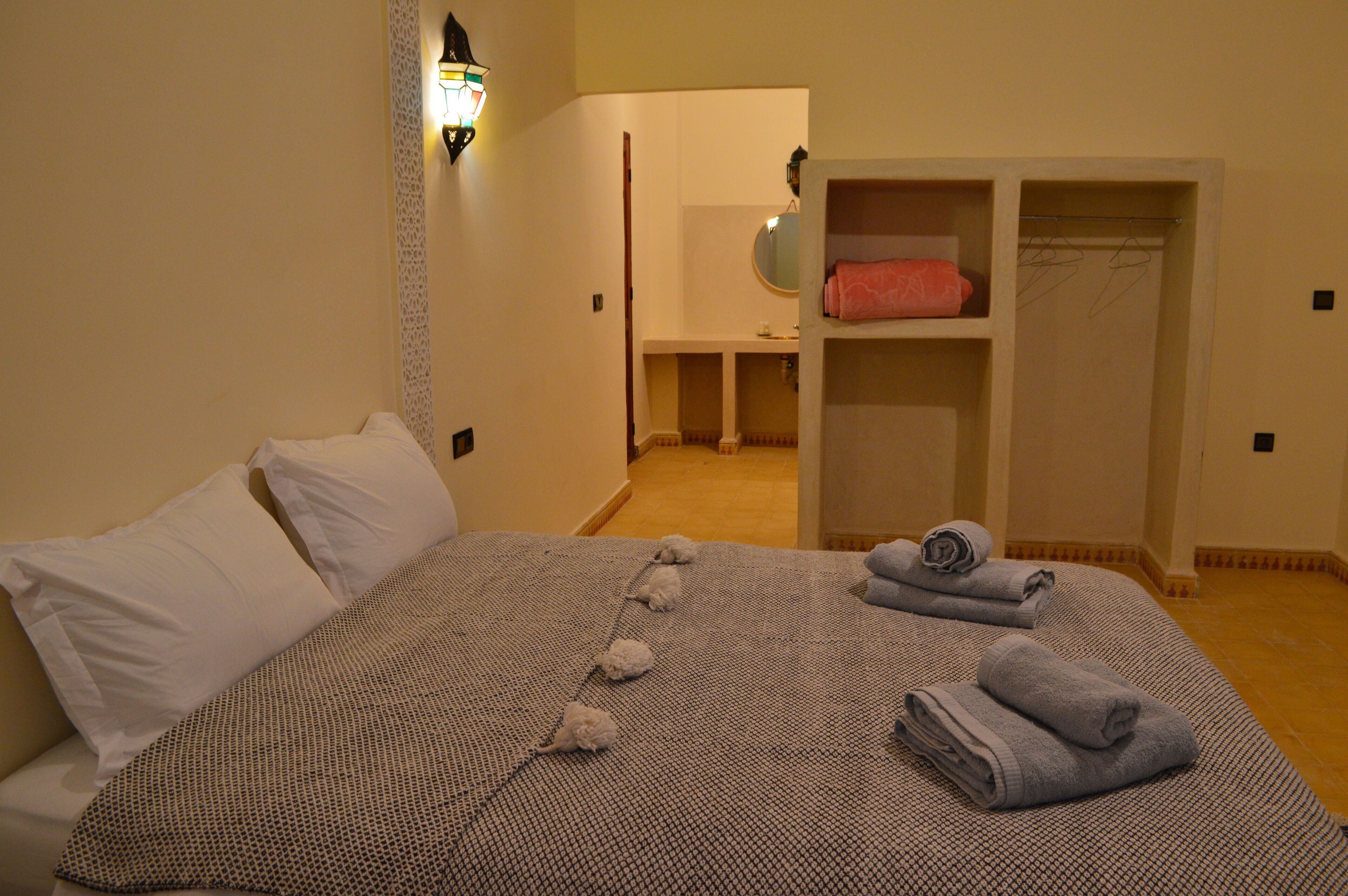 A bedroom with a bed, pillows, a bedside table, a mirror, a wardrobe, and towels.